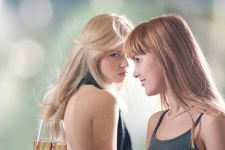 Two women jealously looking at each other with wine glasses in hands