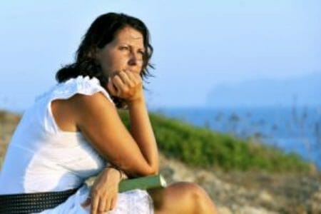 Woman looking into the distance with book on lap and ocean in background