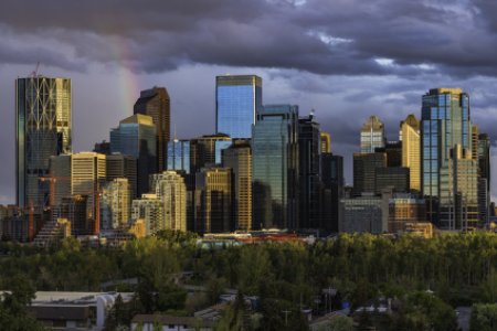 Calgary downtown skyline with dark clouds and small rainbow during sunset