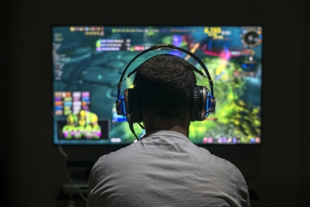 Teenager in front of large screen playing video game with headphones on