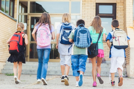 Kids with backpacks walking towards school entrance doors