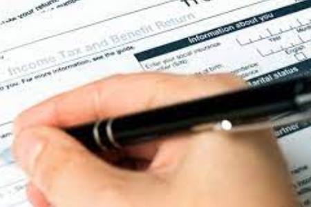 Image of person's hand with a pen filling out a tax form